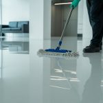 A person cleaning shiny epoxy resin flooring in a bright commercial space using a mop.
