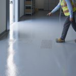 A person wearing safety gear walking on a textured epoxy resin floor in an industrial setting.